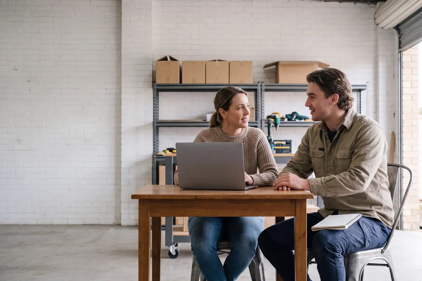 A founder and her first hire talking at a shared desk in a small start-up workspace