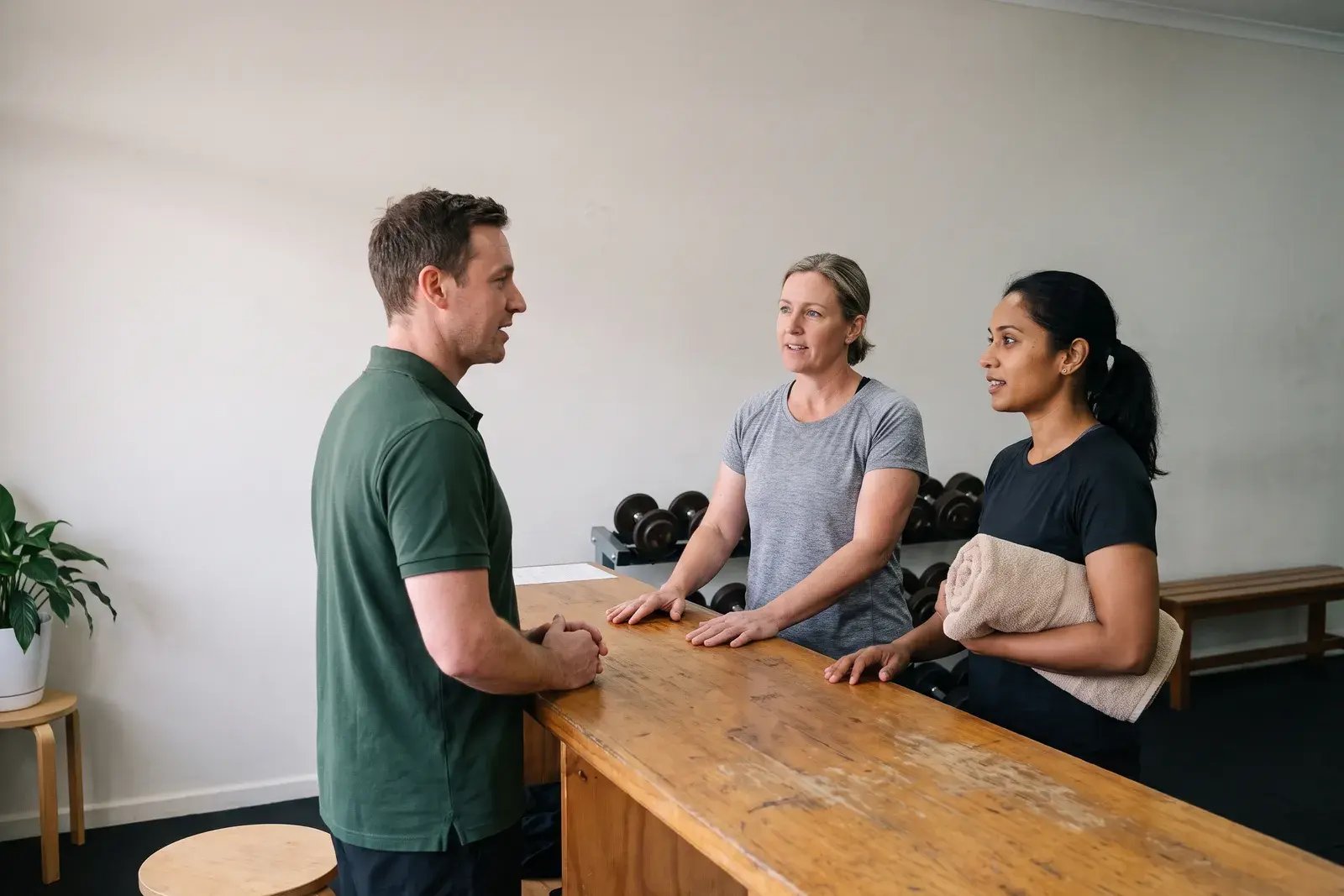A duty manager briefing two instructors at the front desk of a fitness studio